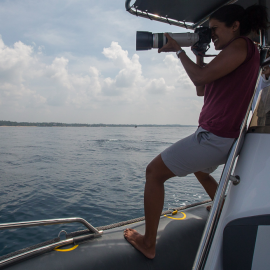 Asha de Vos stood on a boat, using a camera 