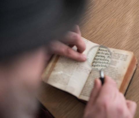 Someone using a magnifying glass to read a small book