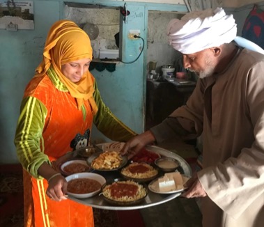 A woman holding a tray with ten different plates of food on it, and a man is steadying one of the plates