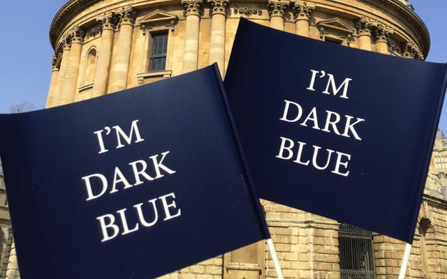 Two 'I'm dark blue' flags waving in front of the Radcliffe Camera