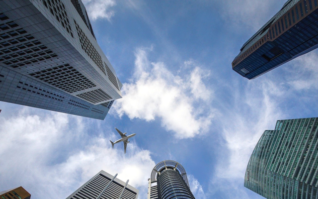 A view from groundlevel vertically upwards through skyscrapers, with an aeroplane flying above them