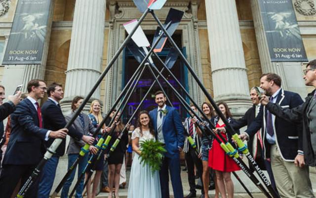 Alex Woods and Zoe de Toledo, on their wedding day, leaving the venue through an arch of rowing oars, lined by wedding guests