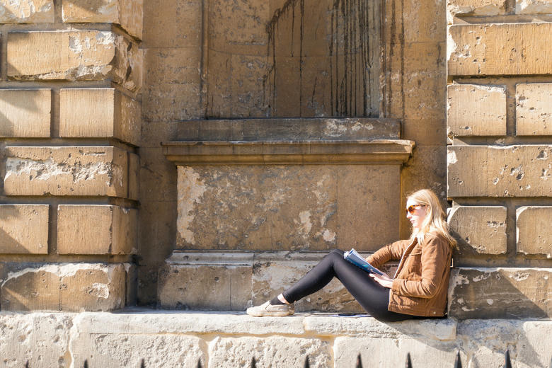 Picture of a young woman reading on a window ledge of the Old Bodleian Library, Oxford