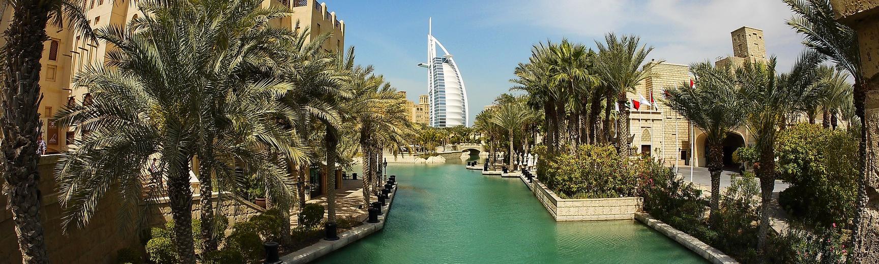 An inland waterway in Dubai, framed by palm trees, with the Burj-al-Arab in the background