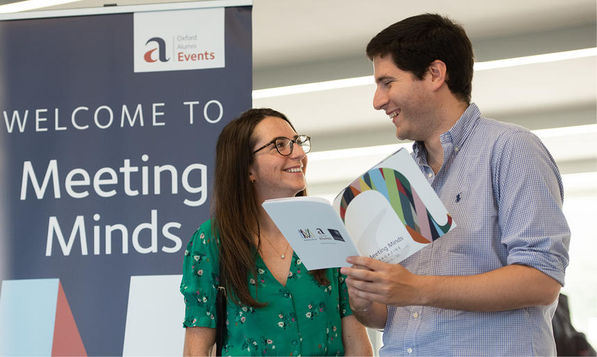 Two attendees looking at a brochure in front of a Meeting Minds pull-up banner