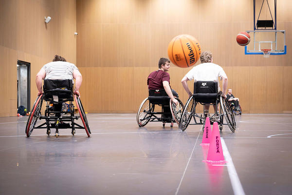 Three members of the Oxford Kites Wheelchair Basketball Club chasing the basketball towards the net