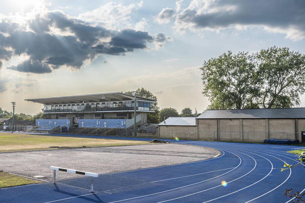 A blue running track, grandstand and dramatic sunlit clouds overhead