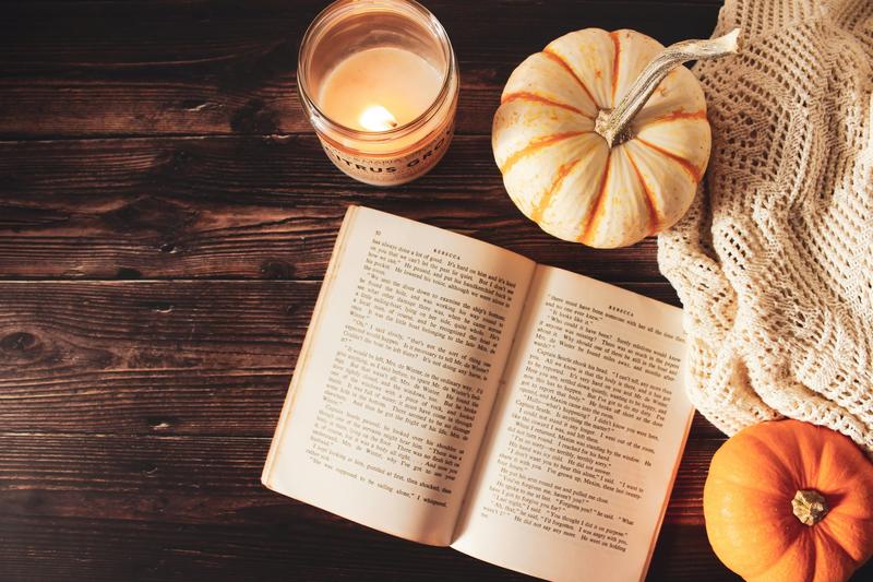 A book lies open next to a lit candle and some small gourds