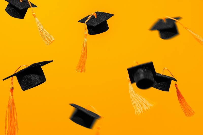 Mortar boards in the air, against a bright orange background