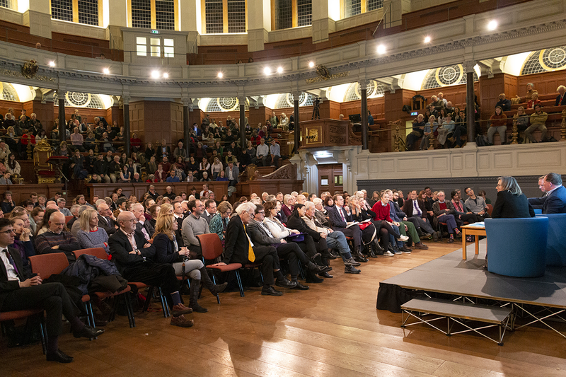 A view from behind the stage of the audience in the Sheldonian Theatre, with the stage and speakers just visible on the right of the picture