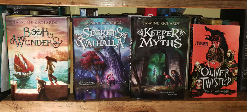 A display of three books by Jasmine Richards - The Book of Wonders, Secrets of Valhalla, Keeper of Myths - next to Oliver Twisted by JD Sharpe