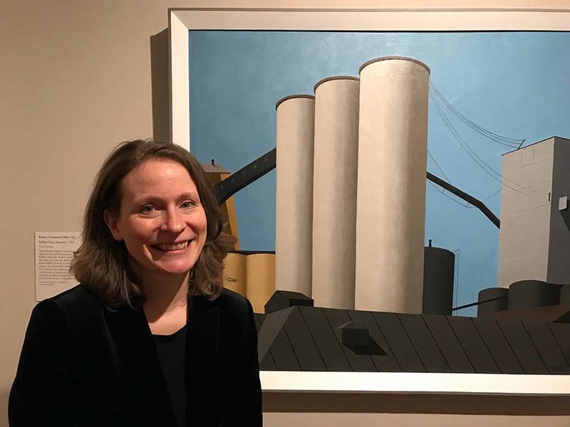 Dr Katherine Bourguignon stood in front of the painting Buffalo Grain Elevators by Ralston Crawford