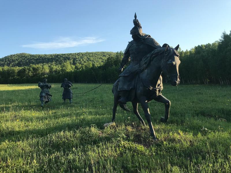 A picture of a statue of Yesugei, Genghis’s father, returning home - it is two people being led across a field by a man on horseback