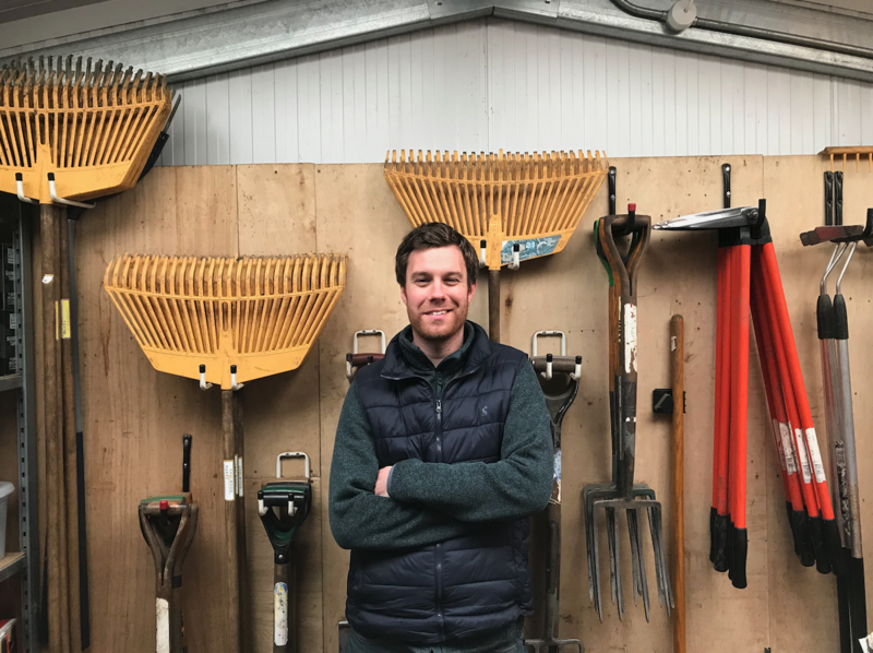 Patrick Green stood in front of a wall on which garden tools are mounted