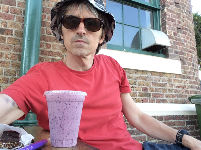 Phil sat at a table, with a purple drink, bruises visble on his right upper arm