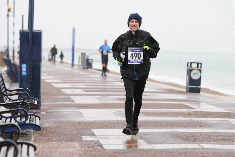Phil Hewitt, dressed for winter weather and wearing a race number, running along a wet seafront