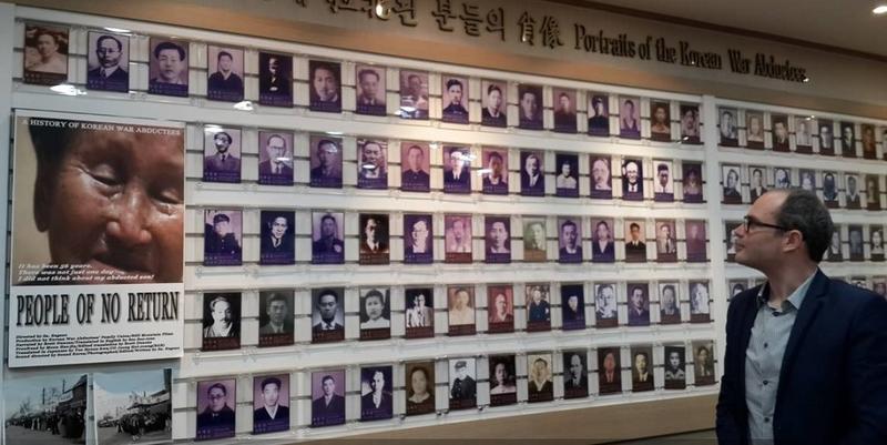 Tarek Cheniti looking at a wall of photos, titled 'Portraits of the Korean War Abductees'