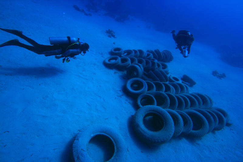 Two divers swimming down to a pile of car tyres on the sea bed