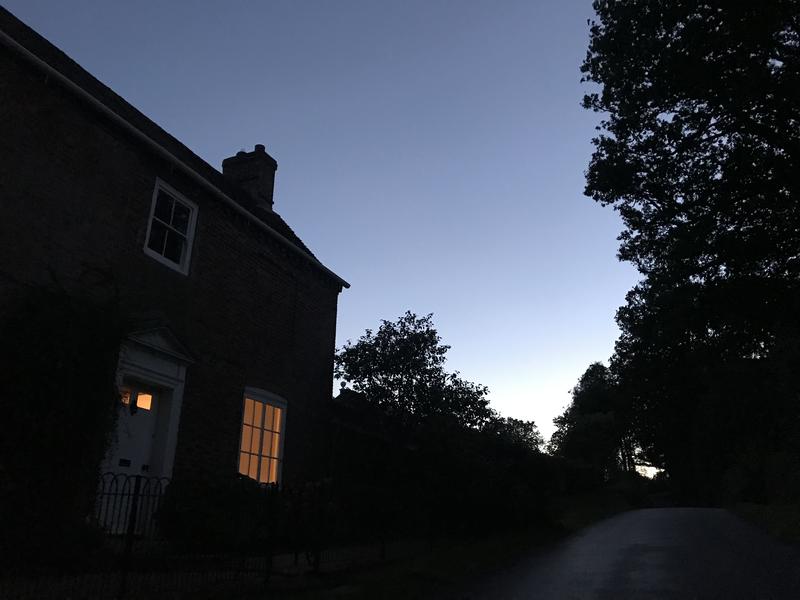 A farmhouse at dusk, with a lighted window