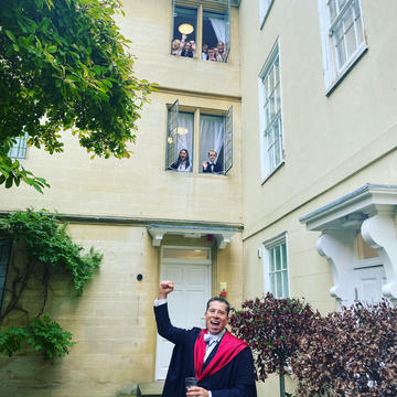 Tom Fletcher raising a fist in the air and cheering. Students looking out of the window above him watching.